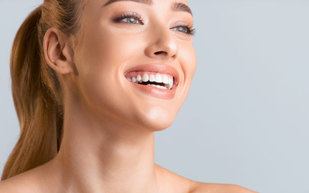 girl smiling largely with white veneers. straight teeth on plain background